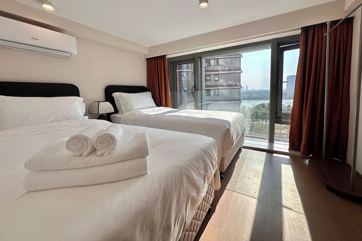 Habitación de hotel con dos camas, un ventanal grande y vistas a la ciudad.