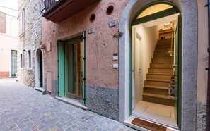 A building with a stone facade, numbered doors, a staircase leading to an upper floor, and a doormat with a family message. - Homestay 'Residenza Tre Cuori' with Lake View, Wi-Fi and Air Conditioning (Torri del Benaco)