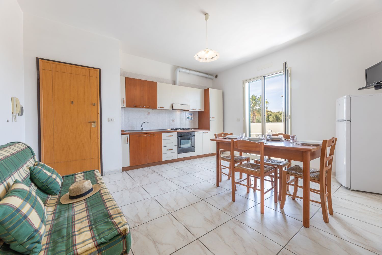 Una cocina moderna con armarios blancos, una mesa de comedor con sillas, un sofá con una manta escocesa y un refrigerador.