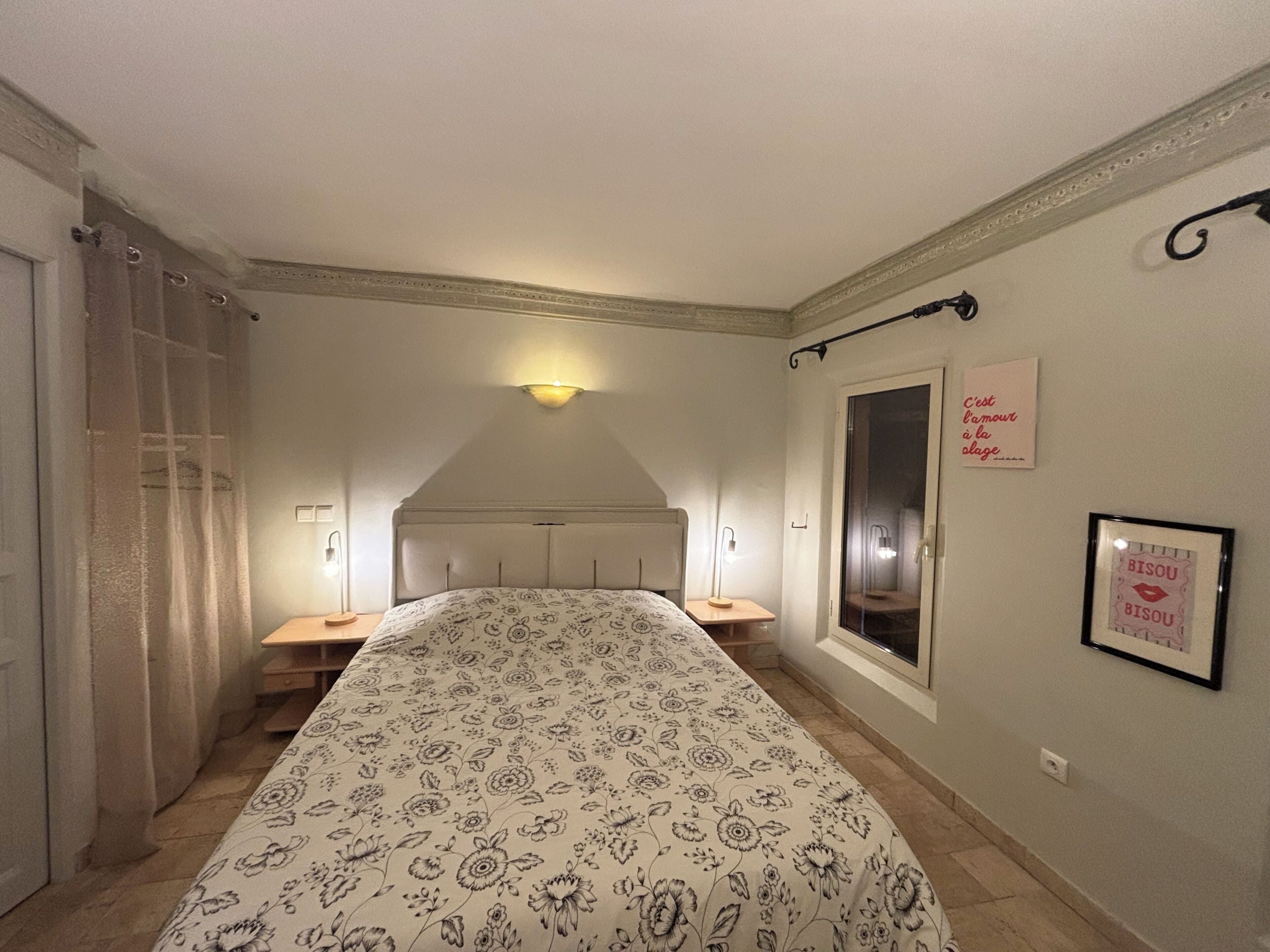 A bedroom with a bed, two bedside tables, a window, and a wall-mounted light fixture.