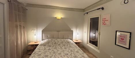 A bedroom with a bed, two bedside tables, a window, and a wall-mounted light fixture.