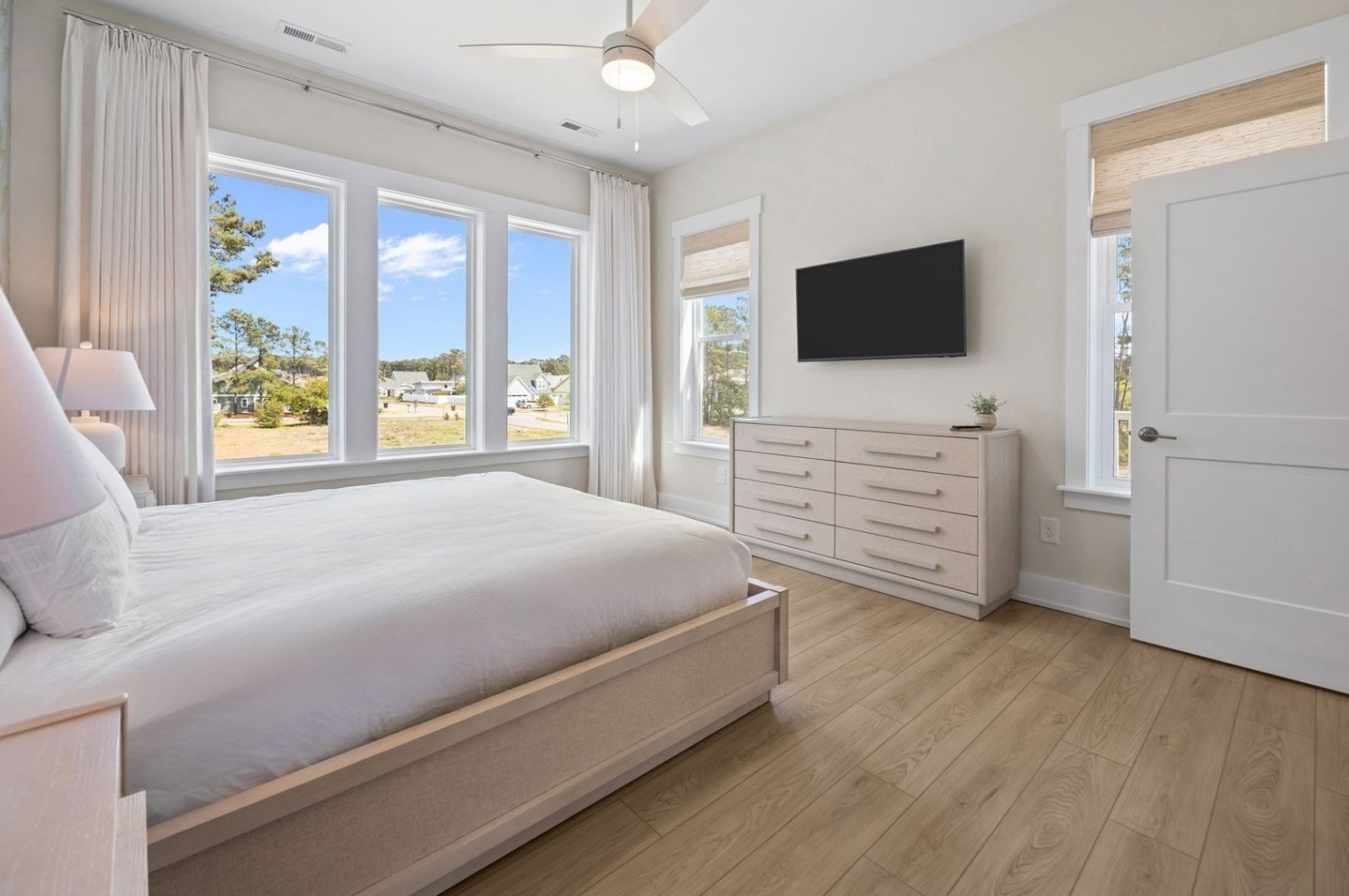 A bedroom with a bed, a TV, a dresser, and large windows.
