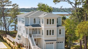A multi-story house with a balcony, a garage, and a view of a lake. - BRAND NEW Saltaire 8 Bedroom Luxury Home at Water Oak (Kill Devil Hills)