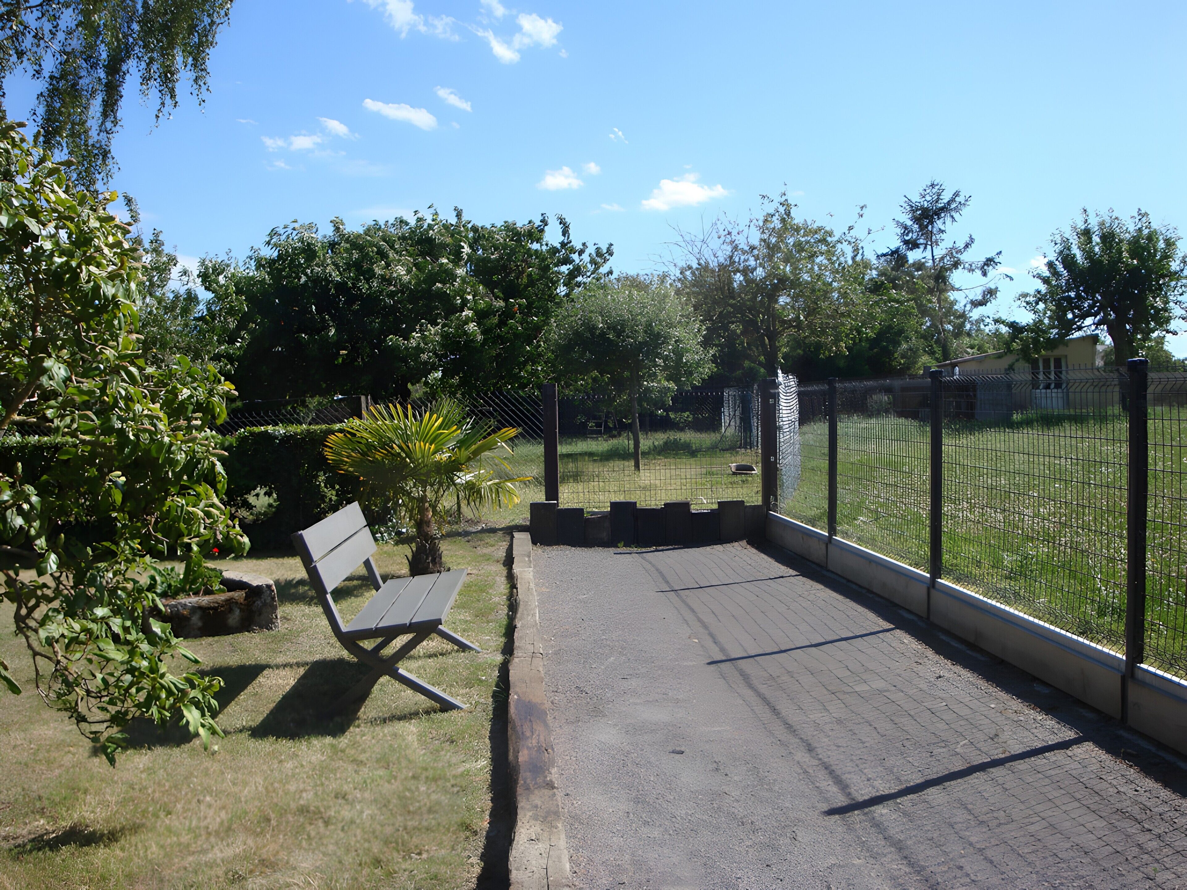 A paved patio area with a bench, surrounded by a fence and greenery.