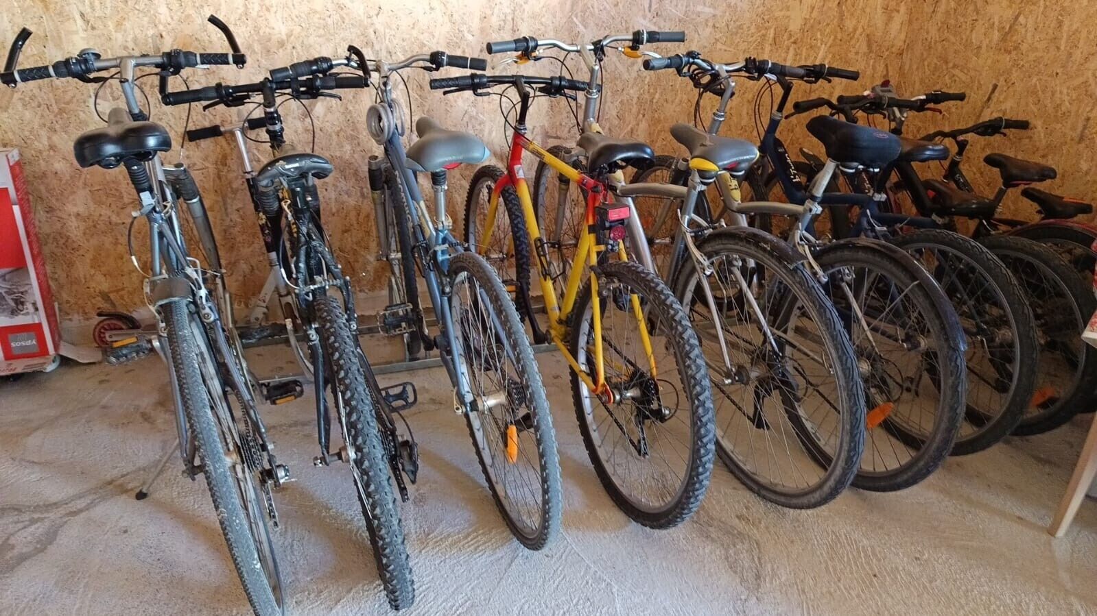 Bicycles parked in a garage with a wooden wall and concrete floor.