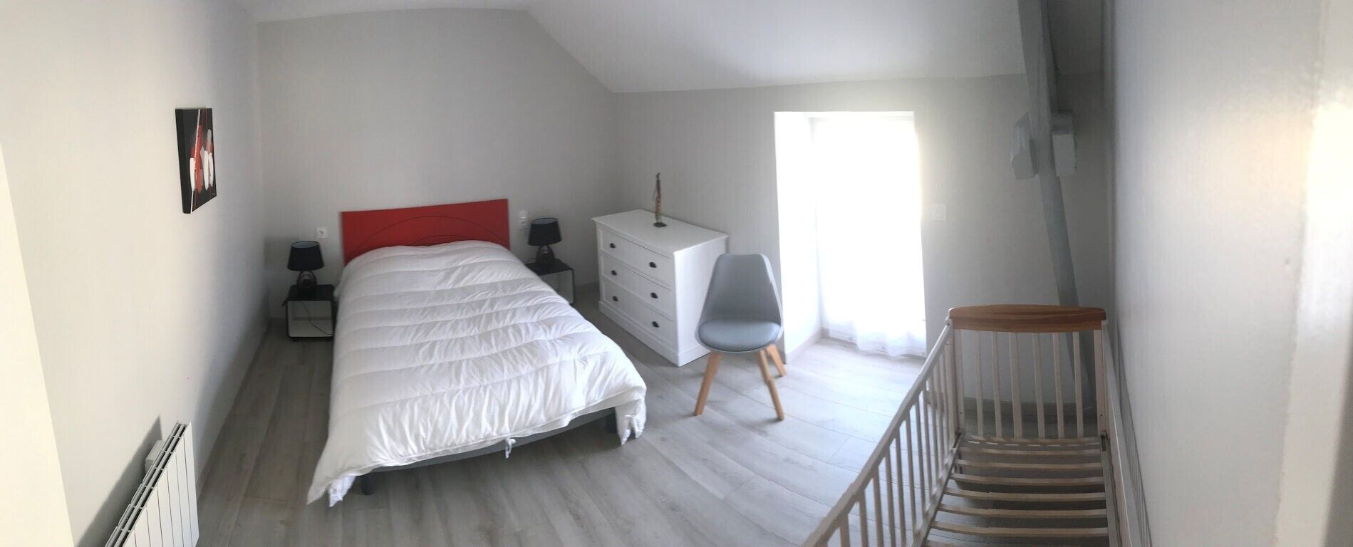 A bedroom with a bed, dresser, chair, and a staircase.