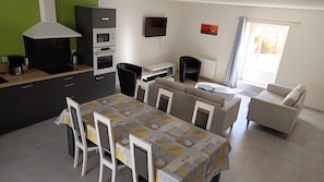 Une cuisine moderne dotée d’un four encastré, une table à manger avec des chaises, un canapé, un téléviseur et une fenêtre avec des rideaux.