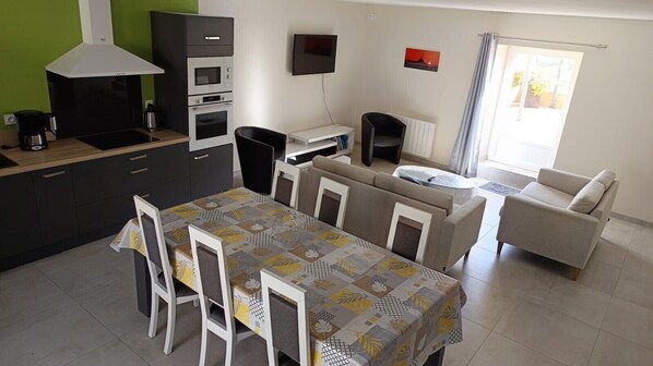 Une cuisine moderne dotée d’un four encastré, une table à manger avec des chaises, un canapé, un téléviseur et une fenêtre avec des rideaux.