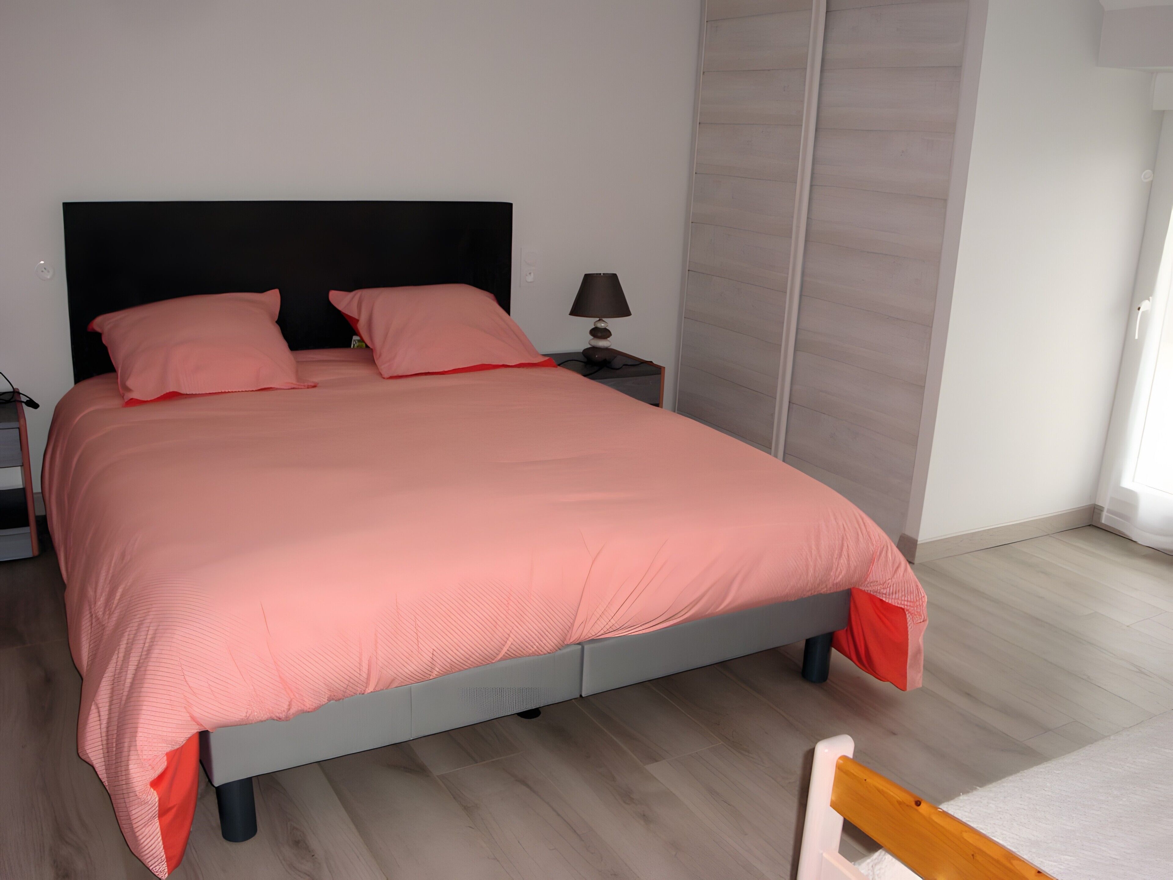 Ein Bett mit Kopfteil, ein Nachttisch mit Lampe und ein Holzboden.