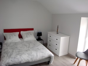 Une chambre à coucher avec un lit, une commode, une chaise et une table de chevet.