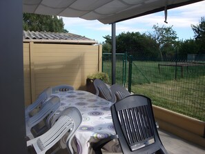 Un patio couvert avec une table et des chaises, un petit abri de jardin et une cour clôturée.