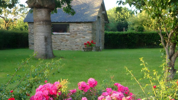 A stone building with a sloped roof, surrounded by a well-maintained lawn and vibrant pink flowers. - Vacation Rental in Beauvoir with Wi-Fi, Family-Friendly, Pets Welcome (Beauvoir)