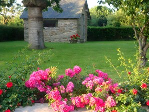 Un bâtiment en pierre doté d’un toit en pente, entouré d’une pelouse bien entretenue et de fleurs roses éclatantes.