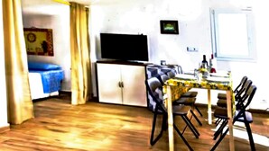 A compact room with a bed, a television, a dining table with chairs, and a small cabinet. - The Attic on the Green (Sicilia)