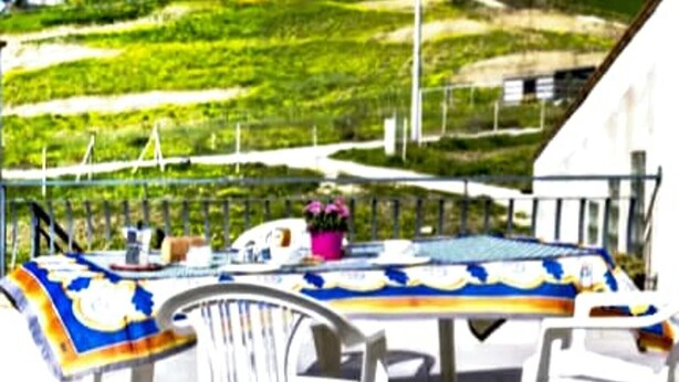 A terrace with a table and chairs, a railing, and a view of green fields. - The Attic on the Green (Sicilia)