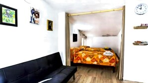 A room with a black sofa, a bed with a patterned bedspread, a clock on the wall, and a framed picture. - The Attic on the Green (Sicilia)