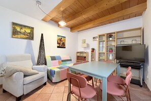Een woonkamer met een bank, een tafel met stoelen, een televisie en een boekenkast.