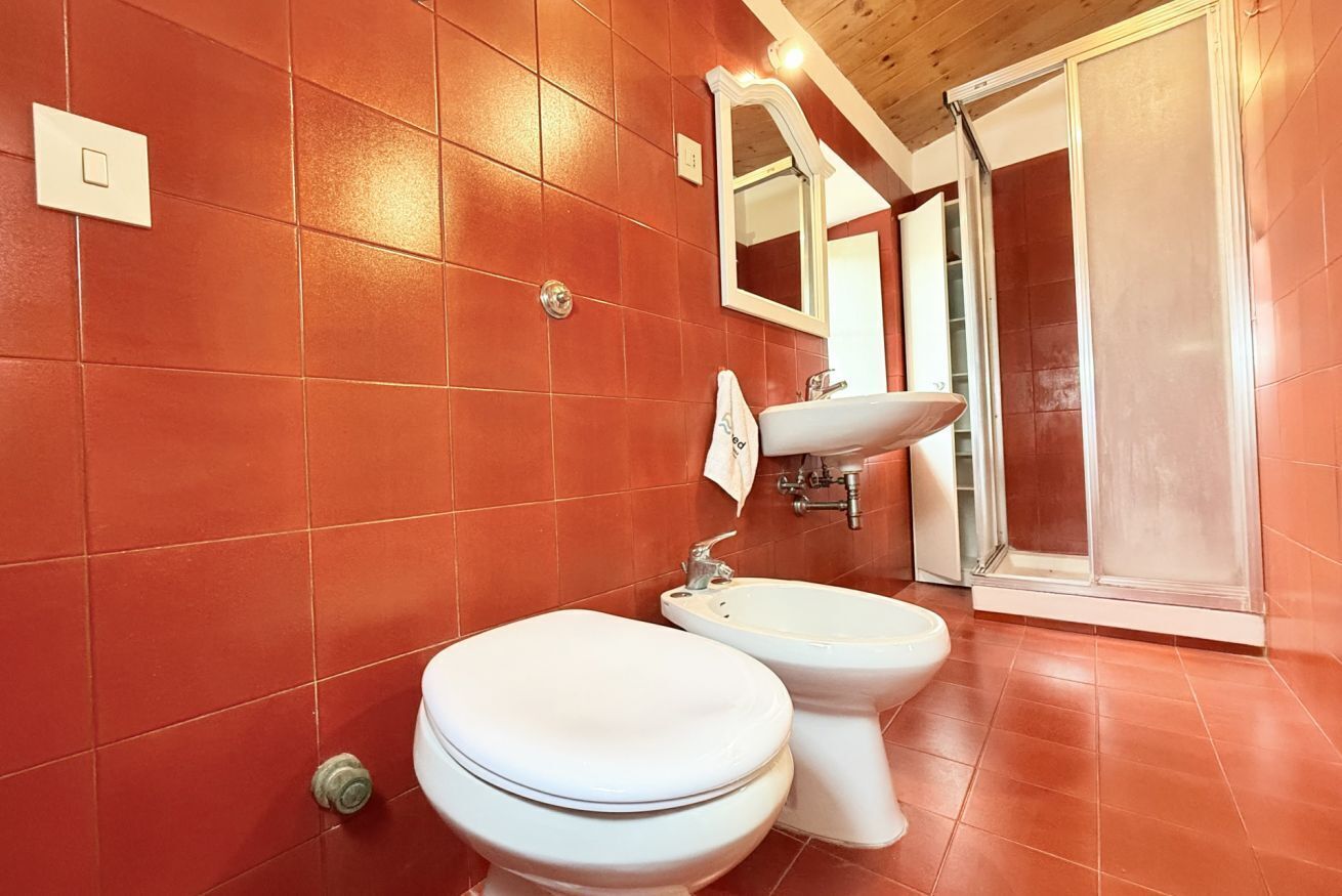 A bathroom with red tiles, a toilet, a bidet, a sink, a mirror, and a shower.