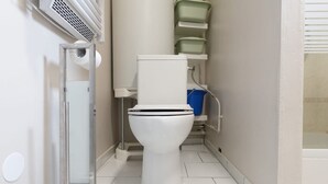 Un inodoro blanco con la tapa bajada, un dispensador de papel higiénico y un cubo de basura azul.