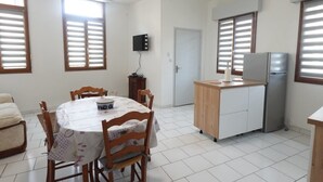 Un comedor con una mesa redonda, sillas, un refrigerador y un televisor montado en la pared.