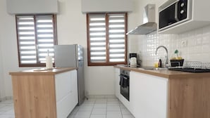 Cocina compacta con una isla de madera, horno empotrado, microondas y una ventana con persianas.