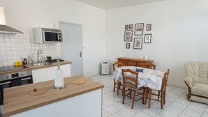 Cocina compacta con microondas, pileta y hornilla, un comedor con mesa y sillas, y un pequeño espacio de descanso con una silla.