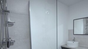 Ein modernes Badezimmer mit Duschkabine aus Glas, einem weißen Waschbecken und einem Spiegel.