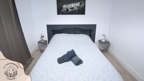 Ein ordentlich bezogenes Bett mit einem gemusterten Bettüberwurf, einem gefalteten Handtuch und einem gerahmten Bild mit der Aufschrift 'Hollywood' an der Wand.