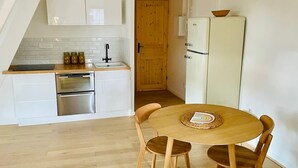 A compact kitchen with white cabinets, a stainless steel oven, and a wooden dining table with chairs. - Appartement Lumineux Scandinave - Coup de Foudre (Arras)