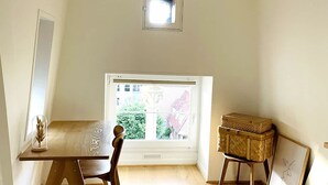 A spacious room with a large window, a wooden table, a chair, a hanging light fixture, and a small window above the table. - Appartement Lumineux Scandinave - Coup de Foudre (Arras)