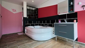 Ein modernes Badezimmer mit einer großen Badewanne, einem Waschtisch mit Schubladen, einem Spiegel und einem Ablagebereich für Pflegeprodukte.