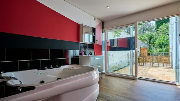 Ein modernes Badezimmer mit einer großen Badewanne, einer Glasdoor zu einer Terrasse und einer Farbgestaltung in Rot und Schwarz.