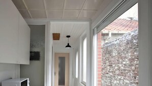 Ein schmaler Gang mit weißer Decke, einer Tür am Ende und einem Fenster zur rechten Seite.