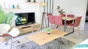 Ein modernes Wohnzimmer mit Fernseher, Esstisch, Stühlen und Topfpflanzen.