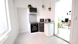 Eine kleine Küche mit Mikrowelle, Backofen und Kaffeemaschine. Hängende Pflanzen und eine gemusterte Spritzschutzleiste sind vorhanden.