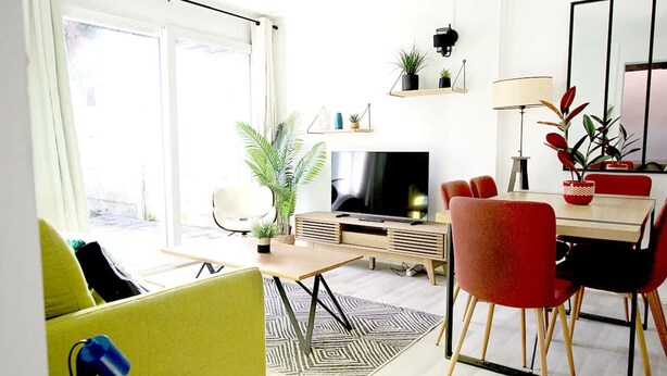 Ein modernes Wohnzimmer mit Fernseher, Essbereich und großen Fenstern.