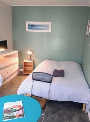 A bedroom with a bed, a nightstand with a lamp, a dresser, and a framed picture on the wall.