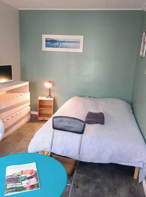 Een slaapkamer met een bed, nachtkastje met een lamp, een dressoir en een lijst met een afbeelding aan de muur.