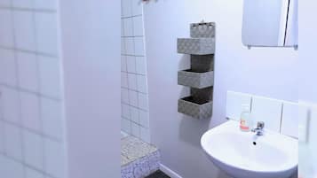Ein Badezimmer mit weißem Waschbecken, einem Spiegel und einer gefliesten Dusche.