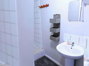 Un baño con lavamanos blanco, un espejo y una zona de ducha con azulejos.