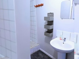 Un baño con lavamanos blanco, un espejo y una zona de ducha con azulejos.
