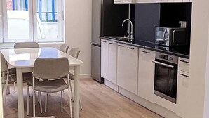 A modern kitchen with a dining area, a built-in oven, and a window with blinds. - Le Cantin 4 Pers Wifi Courette Bollaert (Lens)