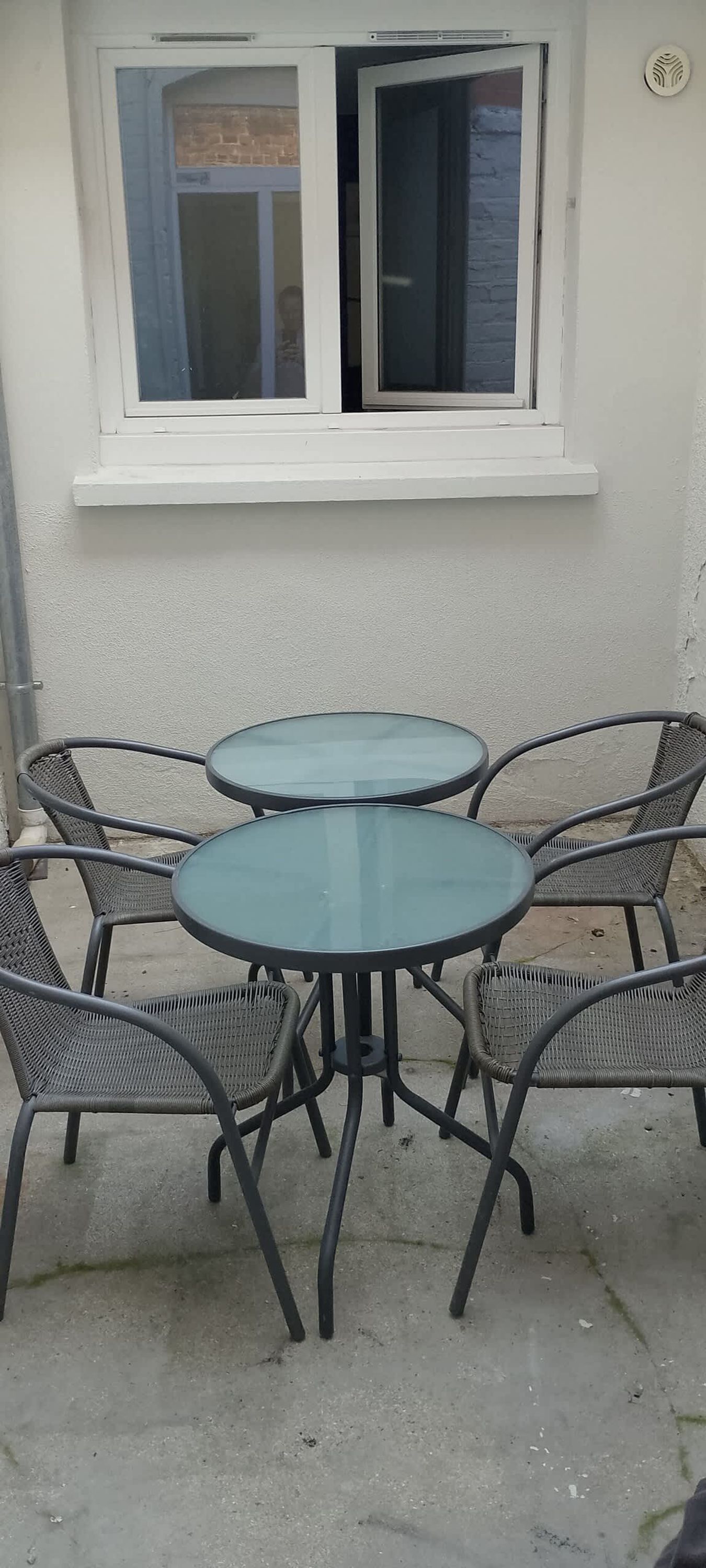 A patio with a round table and six chairs, a window with a white frame, and a white wall.