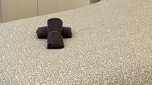 A hotel room with a patterned bedspread, a neatly folded towel, a bedside lamp, and a pillow with a logo. - Le Cantin 4 Pers Wifi Courette Bollaert (Lens)
