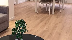 A modern living room with a dining area, a potted plant, and a logo on the floor. - Le Cantin 4 Pers Wifi Courette Bollaert (Lens)