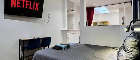 A modern room with a bed, a desk, a chair, a TV mounted on the wall, and a mirror.