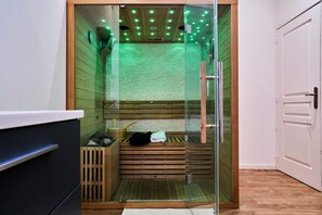 A glass-enclosed sauna with wooden benches, a wooden floor, and a white door. - Baignoire Blaneo Sauna 10 Minutes de la Gare (Tourcoing)