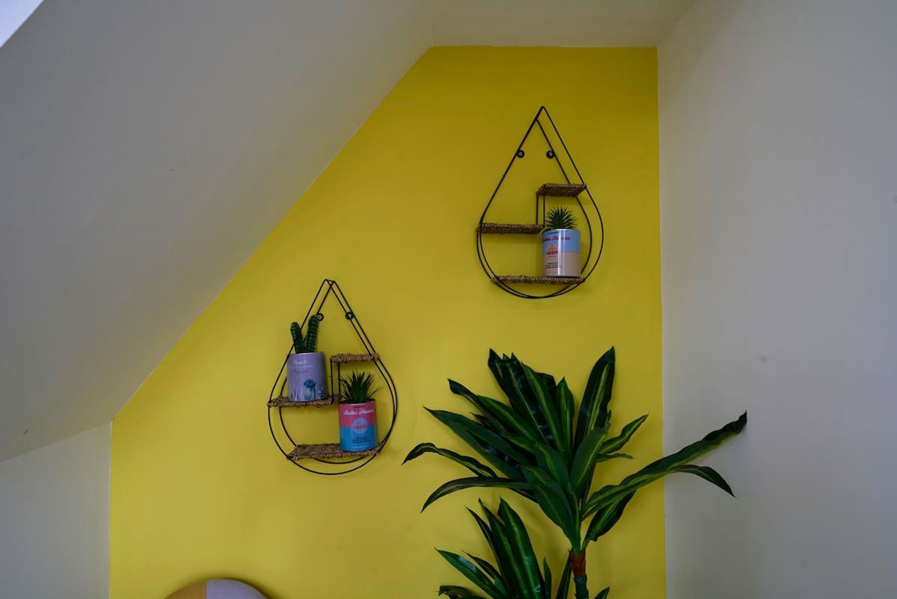 Een gele muur met twee wandplanken voor planten.