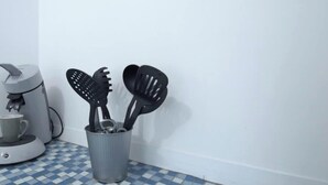Keittiönurkka, jossa on kahvinkeitin, kuppi ja astioiden säilytysastia laatoitetulla lattialla.