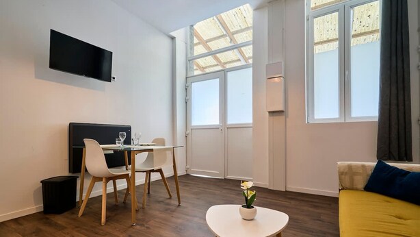 Ein modernes Wohnzimmer mit Flachbildfernseher, Esstisch mit Stühlen, einer Couch und einem kleinen Tisch mit Blumenvase.